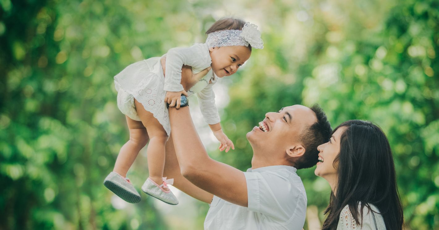 asian parents holding up their baby daughter in the air in an orchard