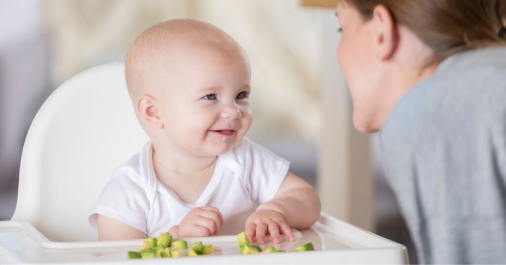 baby is feeding himself avocado and mom is helping him with baby led weaning