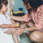smiling mom sitting on the floor, in front of her toddler boy who is sitting on the potty.
